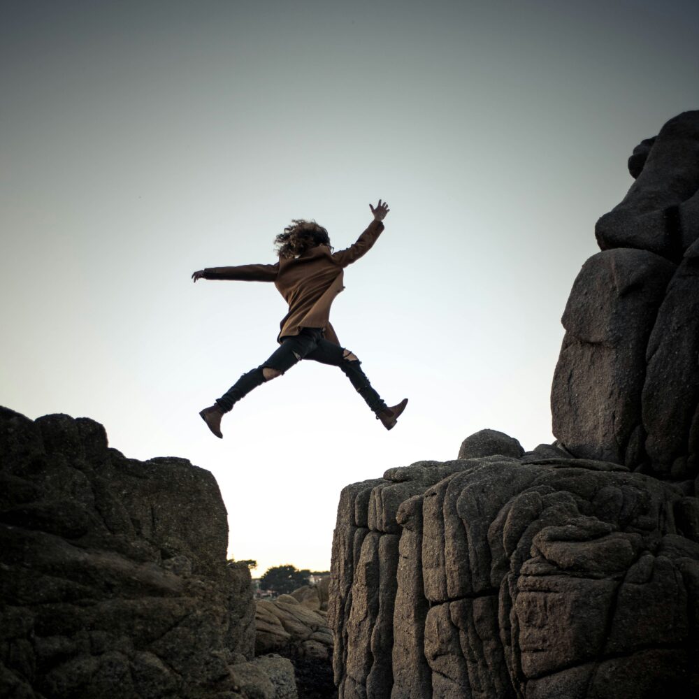 Young person, casually dressed, jumps between Rocks on the seaside